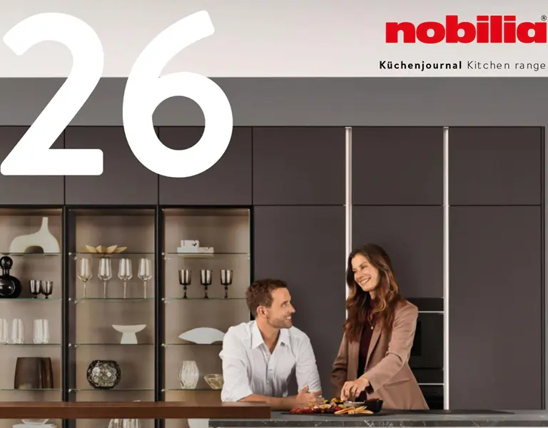 Helle Einbauküche mit glatten Holzoberschränken, weißer Arbeitsplatte in Marmoroptik und goldener Armatur, im Vordergrund eine Frau in beiger Kleidung mit Tasse in der Hand